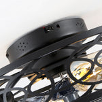 Close up view of the top matte black metal mounting canopy of a ceiling fan showing pre-drilled holes and the upper edge of the geometric iron cage frame